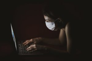 a woman using her laptop while wearing a mask